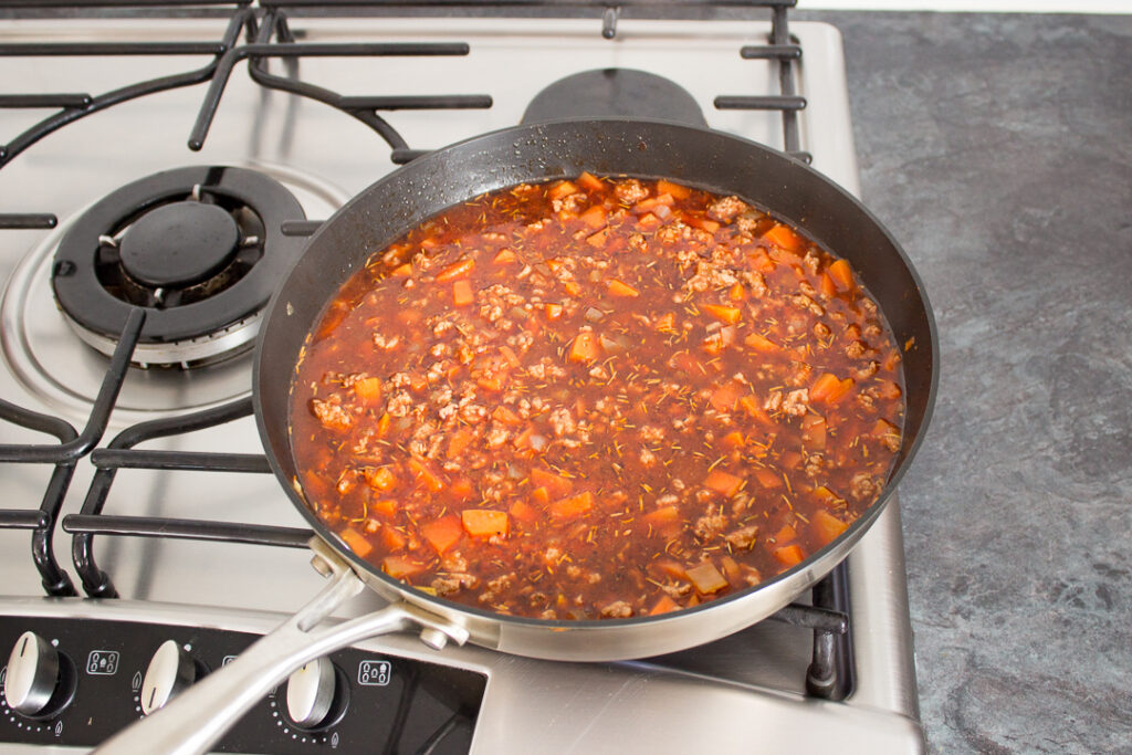 Mince, vegetables, seasonings and beef stock cooking in a large frying pan.