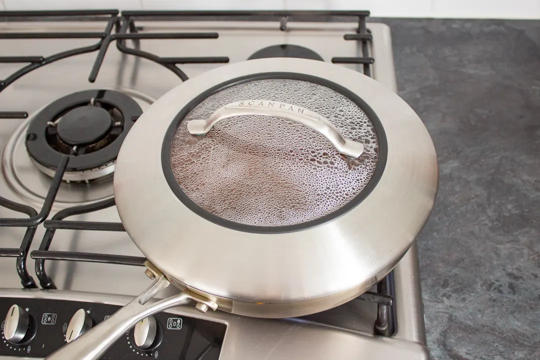 Shepherd's pie mince filling cooking in a large frying pan with a lid on.