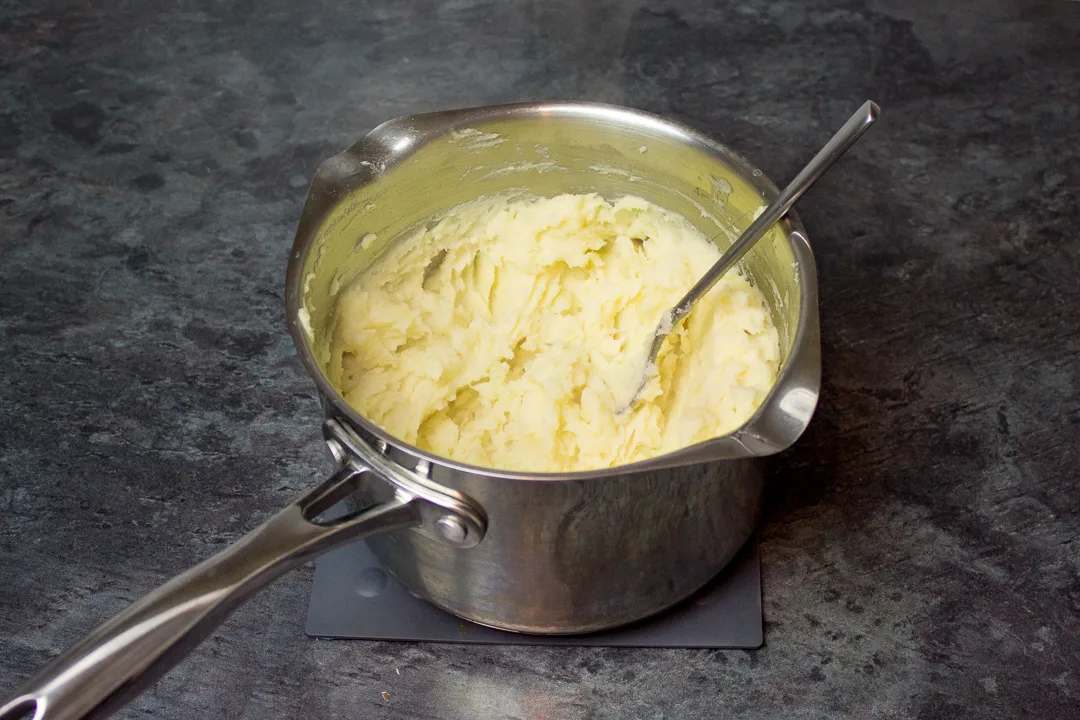 Mashed potatoes in a large saucepan with a fork.