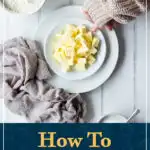 Someone putting a plate of cubed butter down next to flour, eggs and sugar. A text overlay says 'how to soften butter quickly - 4 ways!'.