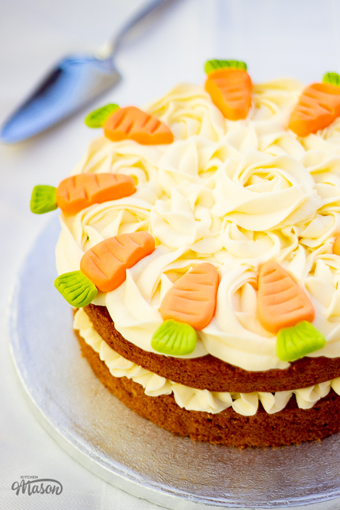 Carrot cake on a cake board topped with carrots sugar decorations.