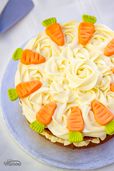 Top down view of a carrot cake on a cake board, decorated with cream cheese icing rose swirls.