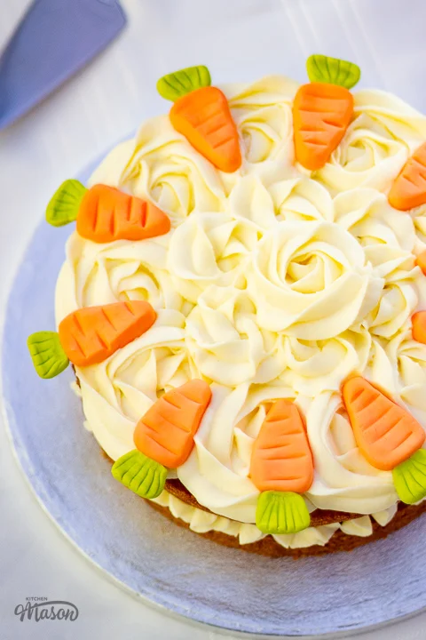 Top down view of a carrot cake on a cake board, decorated with cream cheese icing rose swirls.