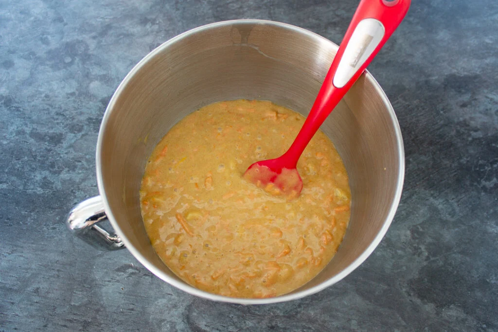 Carrot cake batter in the bowl of an electric stand mixer with a spatula.