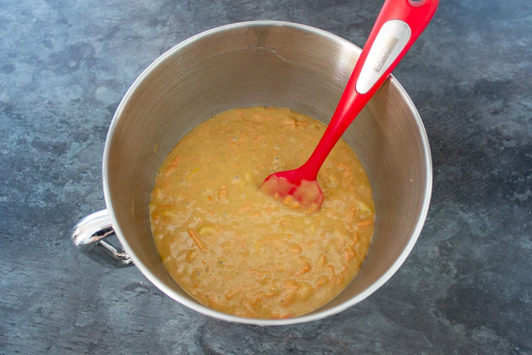 Carrot cake batter in the bowl of an electric stand mixer with a spatula.