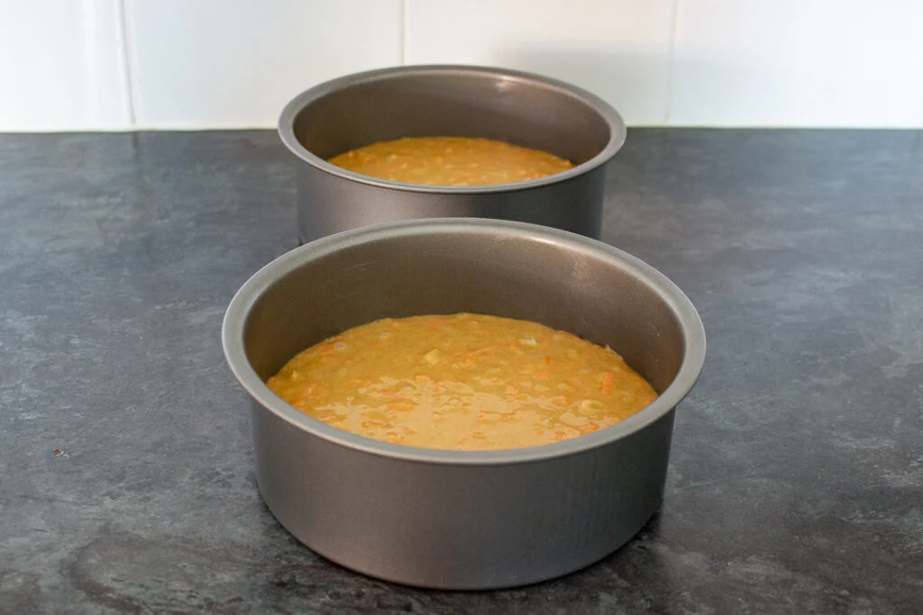 Carrot cake batter divided between two prepared round cake tins.