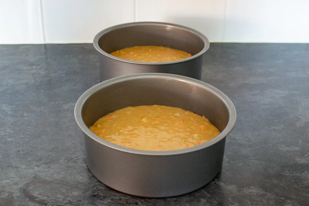 Carrot cake batter divided between two prepared round cake tins.