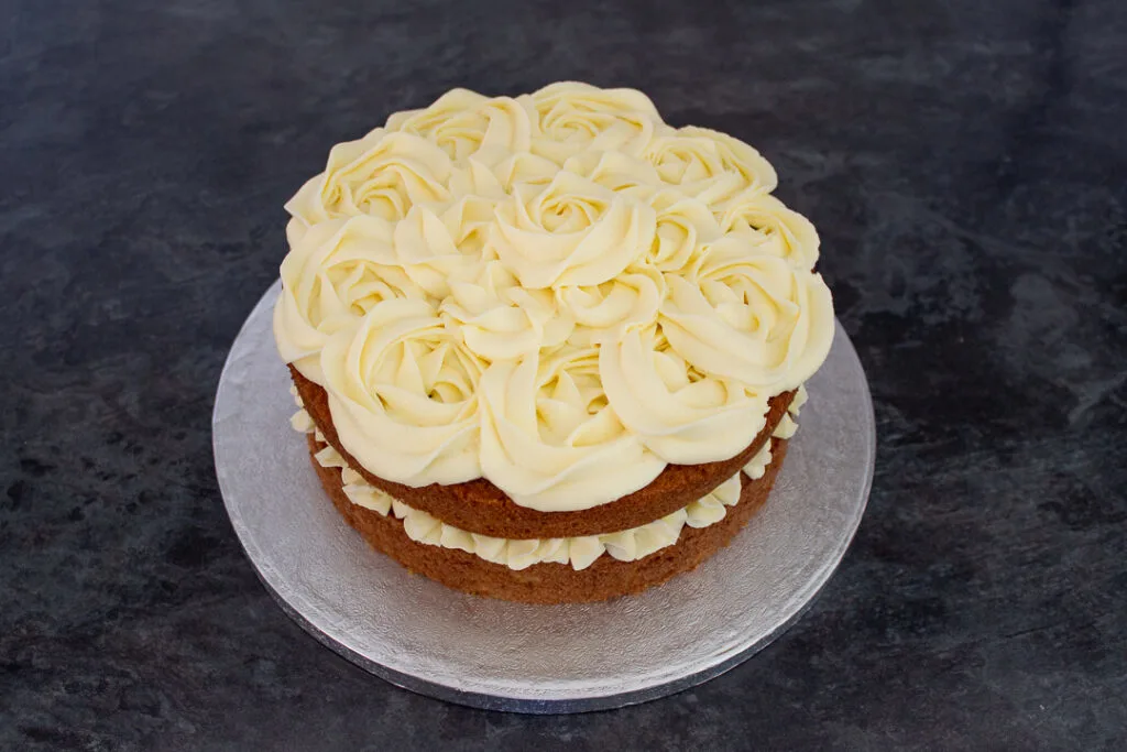 A two layer carrot cake decorated with rose shaped cream cheese frosting swirls.