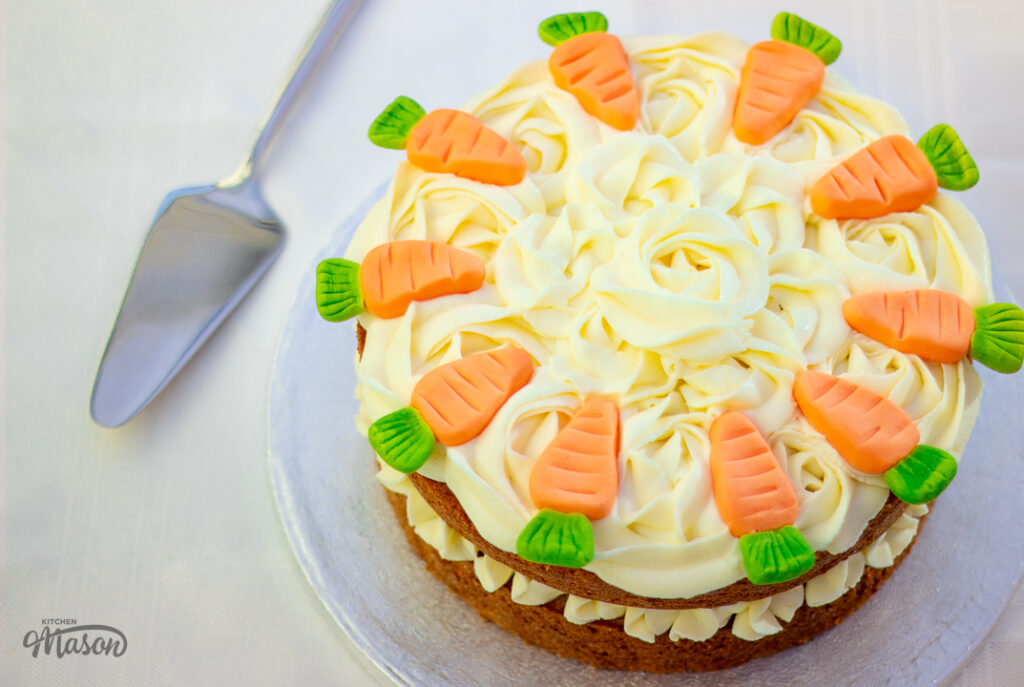 A carrot cake on a cake board with a cake slice next to it.