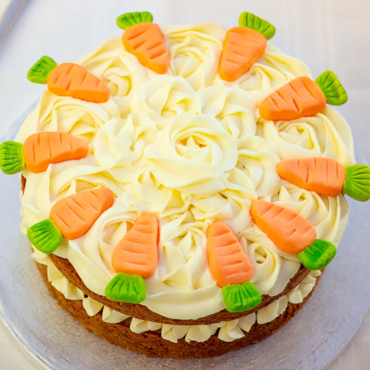 A whole carrot cake decorated with rose shaped swirls and fondant carrots.