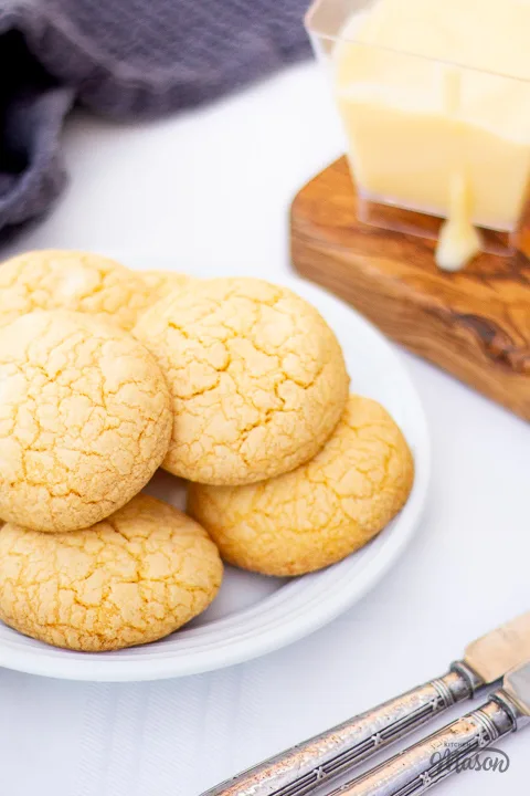 Custard and white chocolate biscuits on a plate with a tea towel and pot of custard to the side.