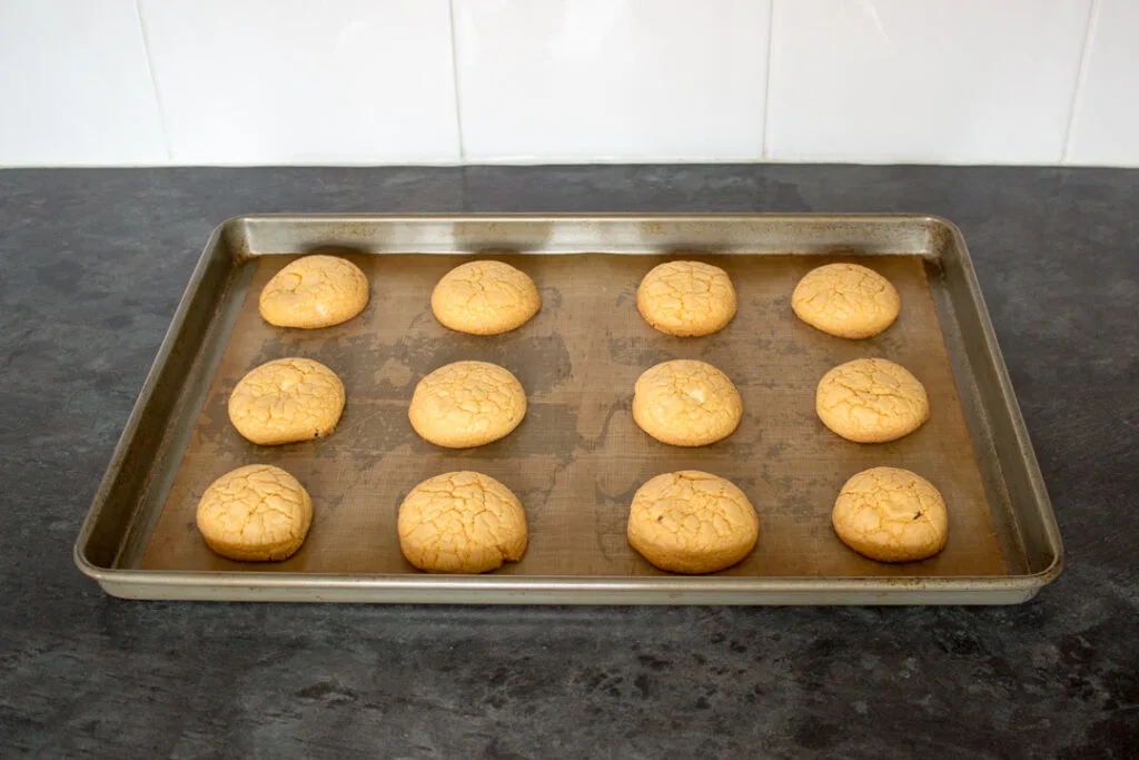 Baked custard and white chocolate biscuits on a lined baking tray.