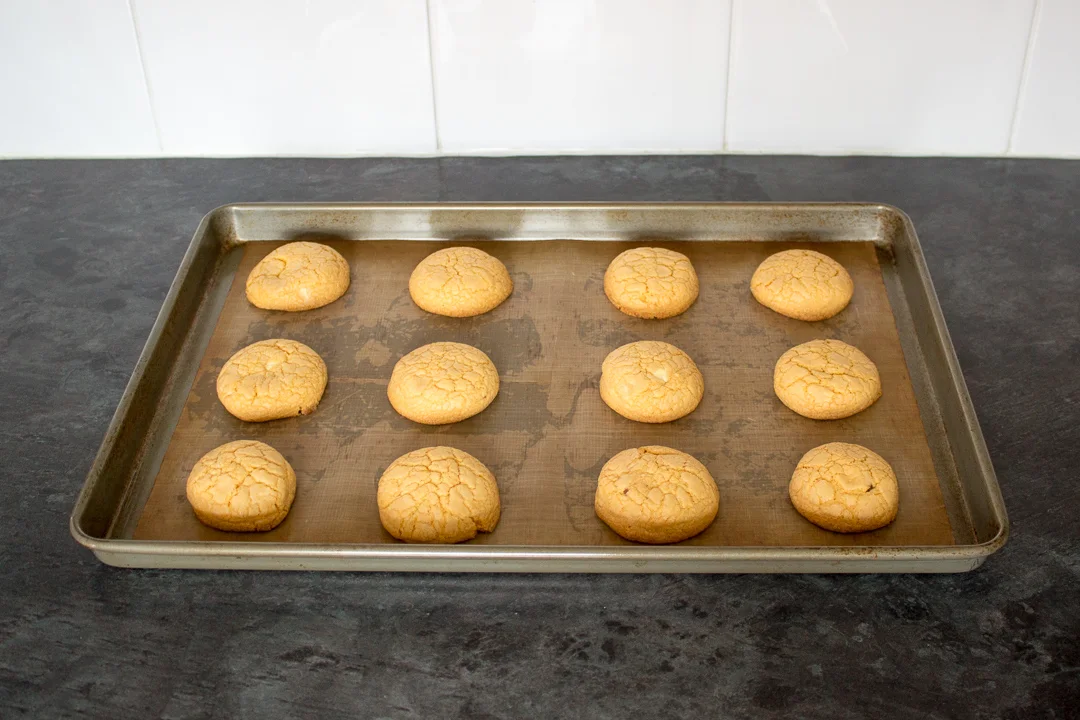 Baked custard and white chocolate biscuits on a lined baking tray.