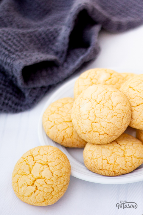 Custard and white chocolate biscuits on a plate with a dark grey tea towel at the side.