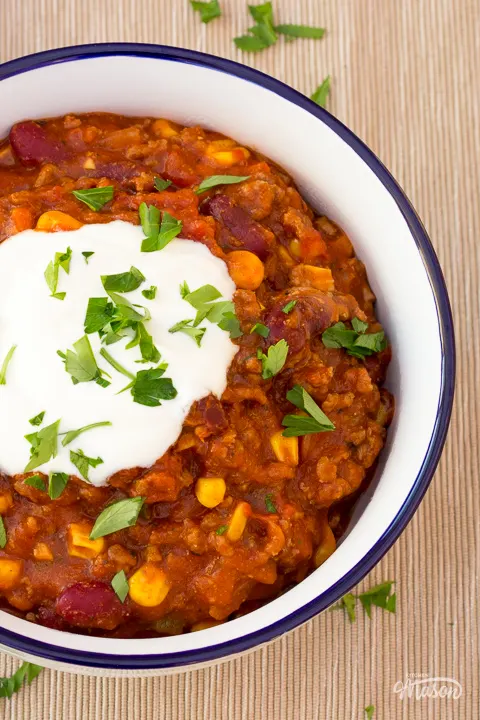 Chilli con carne in a white bowl topped with soured cream and chopped parsley.