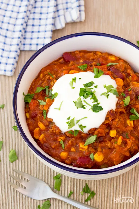 A white bowl filled with homemade chilli con carne, topped with soured cream and parsley.