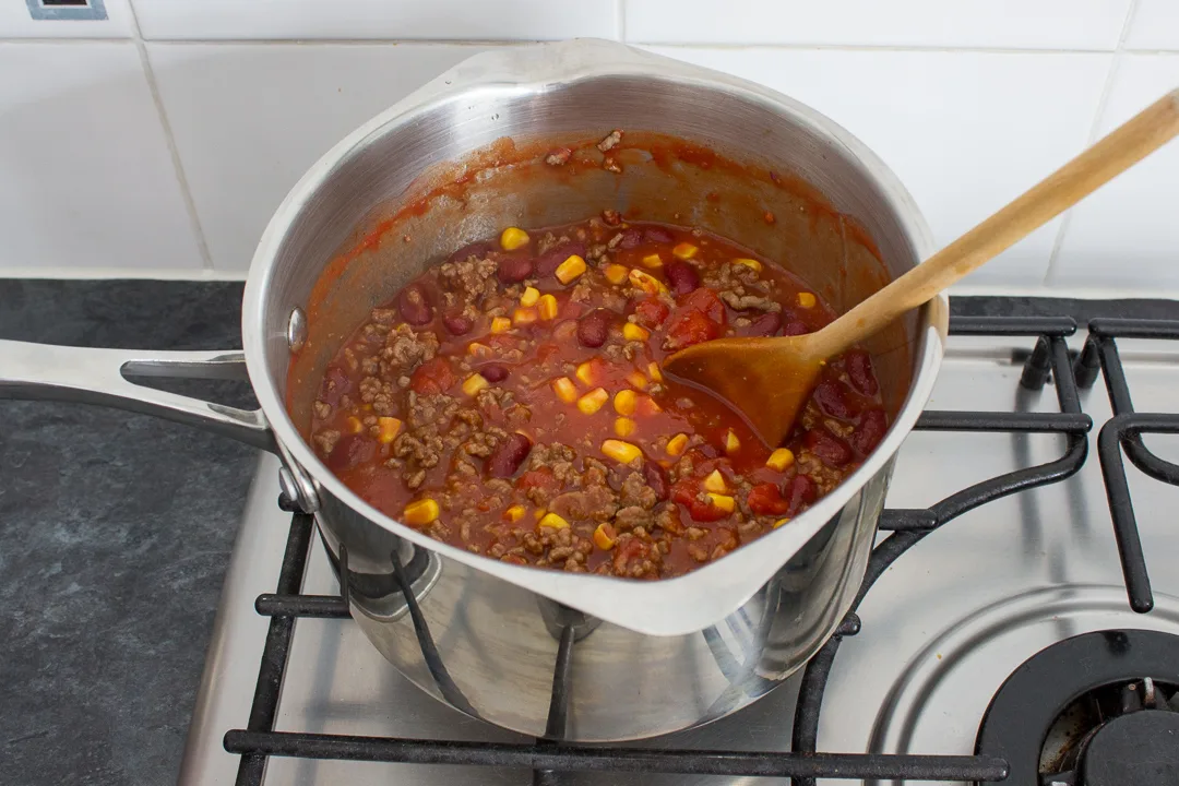 Chilli con carne ingredients in a large saucepan with a wooden spoon.