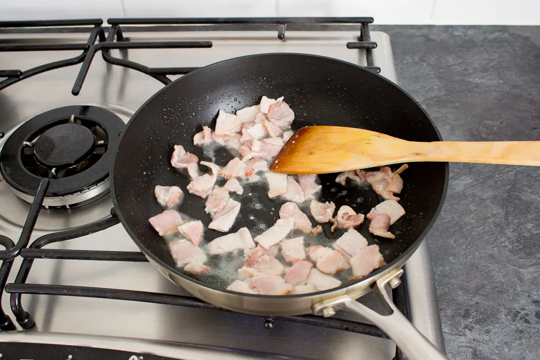 Bacon frying in a large frying pan.
