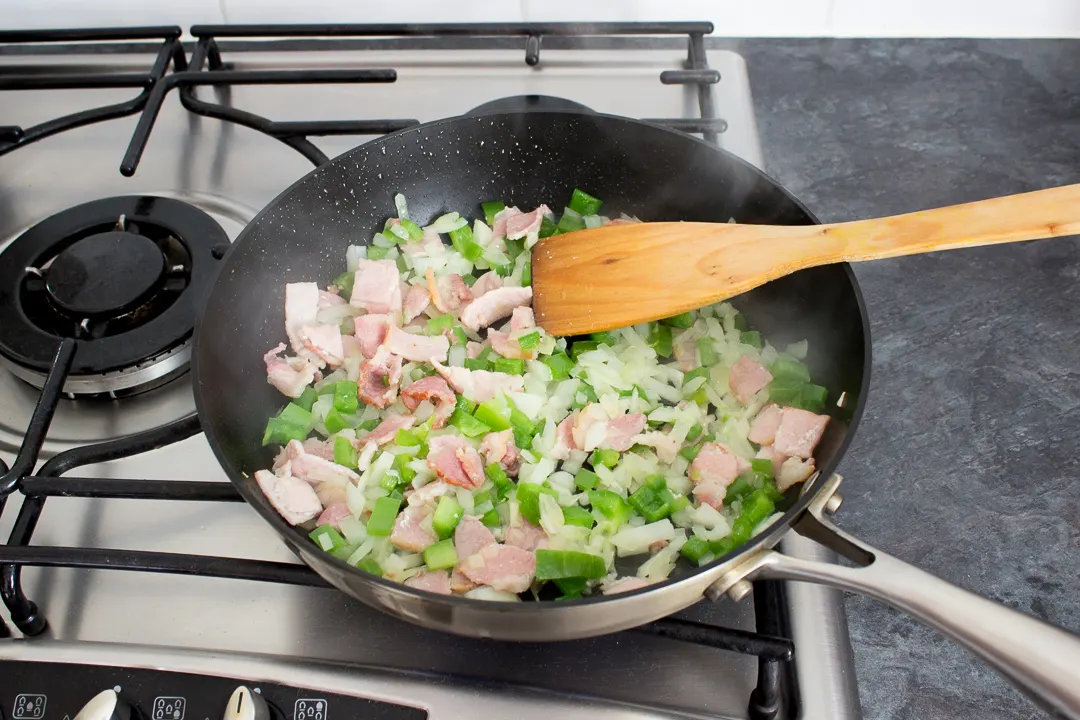 Bacon, onion and peppers frying together in a frying pan.