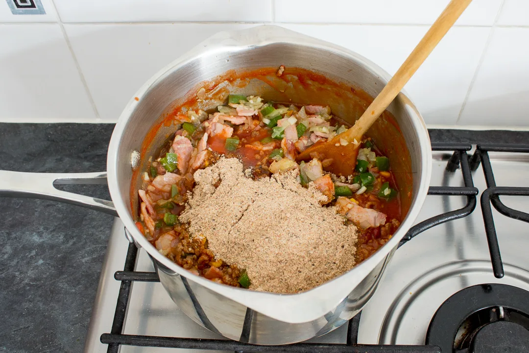 Chilli seasoning being added to the rest of the ingredients in a large saucepan.