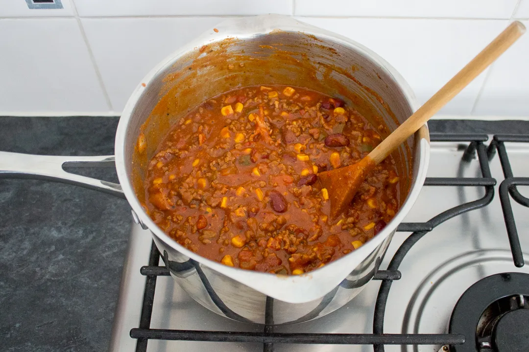 Full cooked chilli con carne in a large saucepan with a wooden spoon.