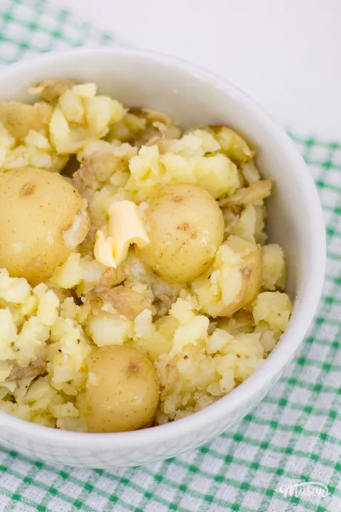Crushed new potatoes and butter in a small white bowl.
