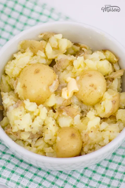 A small white bowl filled with crushed baby potatoes, topped with a knob of butter.