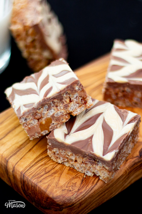 Several slices of Mars Bar slice on a wooden chopping board.