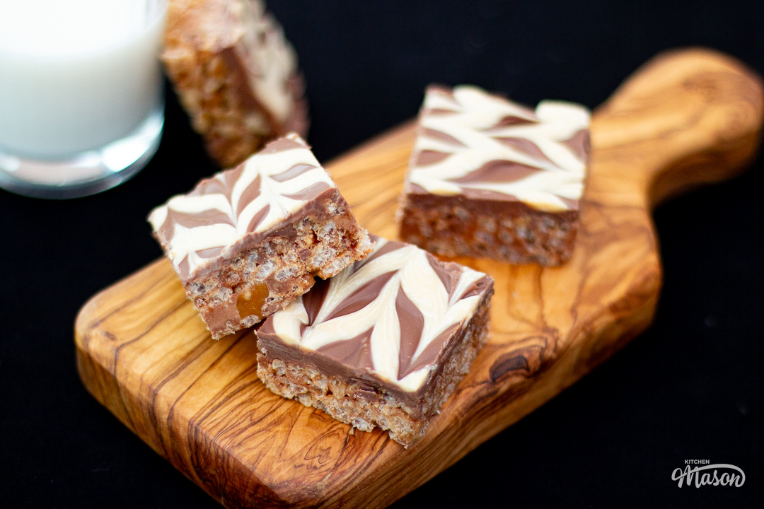 Mars Bar Slice bars on a wooden board, with a glass of milk to the side.