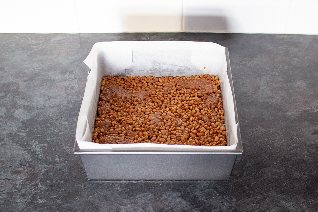 Mars Bar and Rice Krispie mixture pressed into a lined square baking tin.