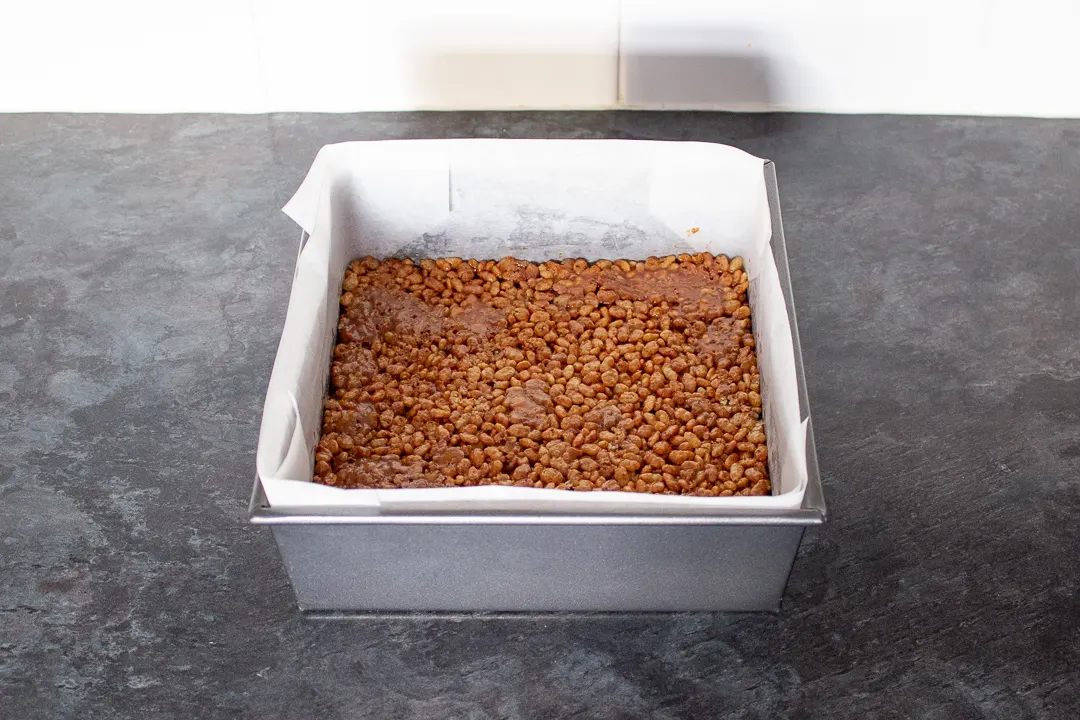 Mars Bar and Rice Krispie mixture pressed into a lined square baking tin.