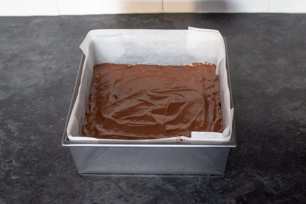 Melted milk chocolate smoothed over the top of a melted Mars Bar and Rice Krispie mixture in a square baking tin.