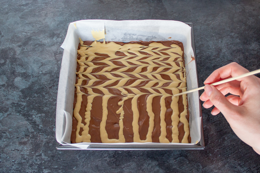 Melted blonde chocolate being feathered on top of the melted milk chocolate.