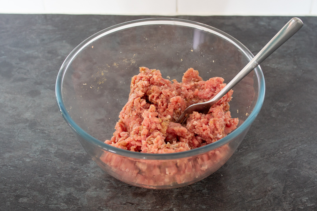 Turkey mince and seasonings in a glass mixing bowl with a fork.