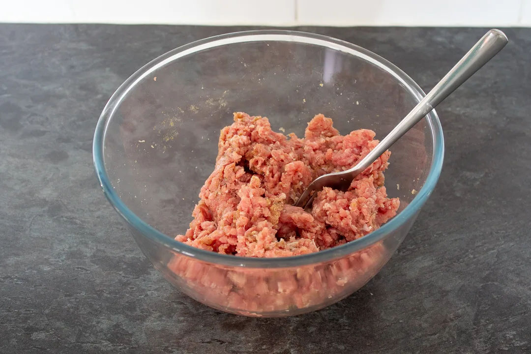 Turkey mince and seasonings in a glass mixing bowl with a fork.