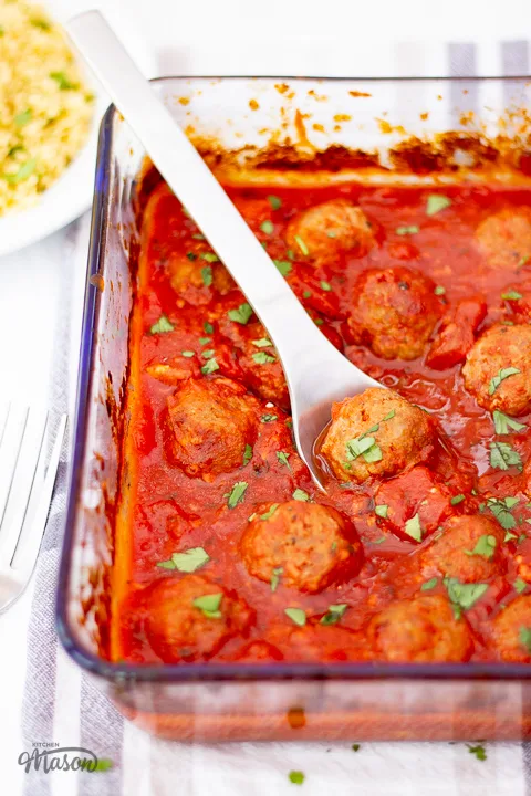 Oven baked tomato turkey meatballs in a glass dish with a metal spoon.