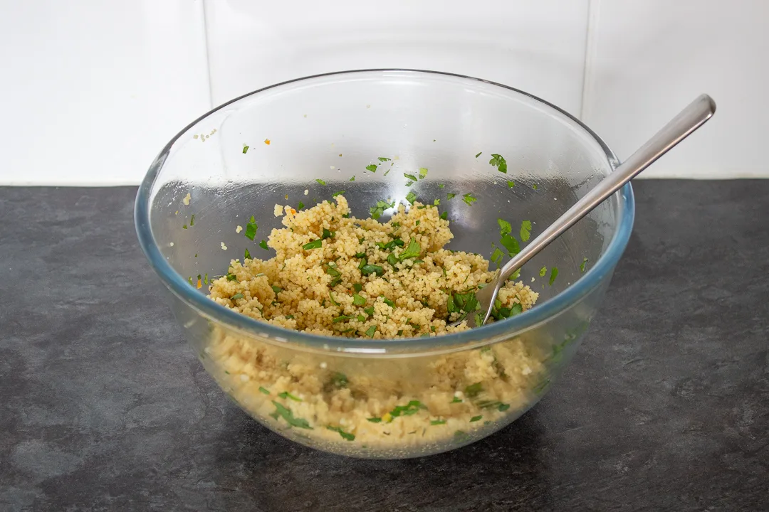Cooked couscous with added seasonings and herbs in a glass mixing bowl.