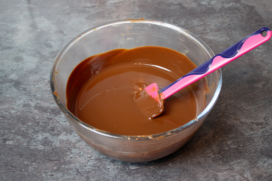 Melted chocolate, butter and golden syrup in a large mixing bowl with a spatula.