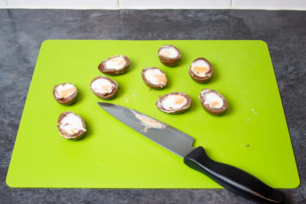 Creme Eggs sliced in half on a chopping board.