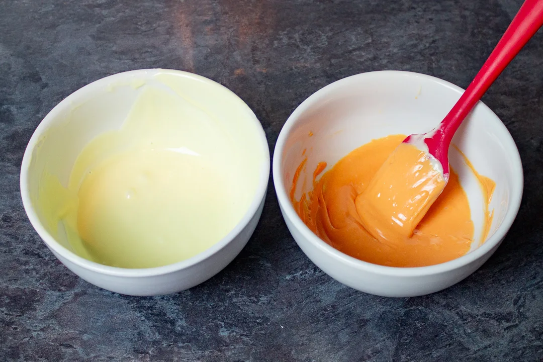 Two bowls, one with melted white chocolate, and another with melted white chocolate dyed orange.