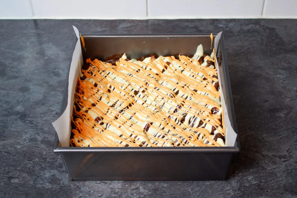 Melted orange coloured white chocolate drizzled over the top of rocky road in a baking tin.