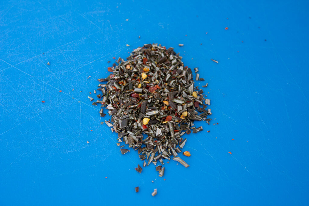 Fresh rosemary and chilli flakes chopped together on a chopping board.