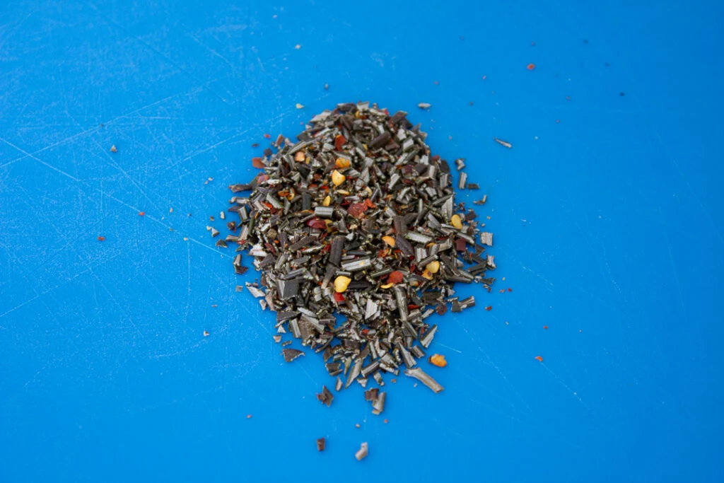Fresh rosemary and chilli flakes chopped together on a chopping board.