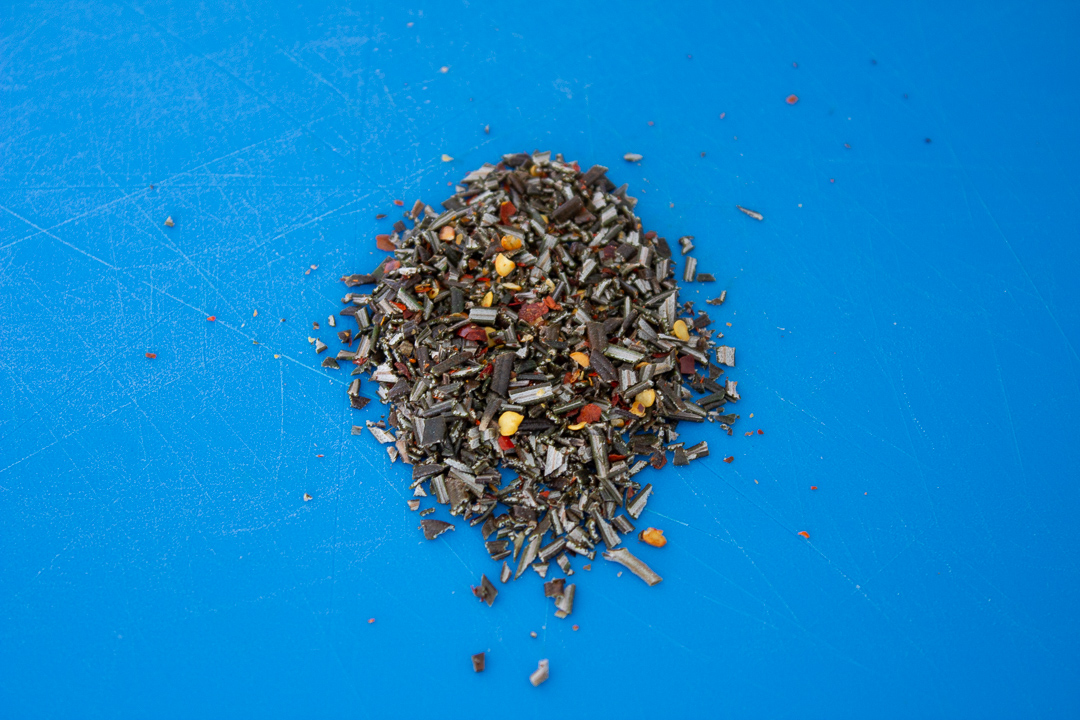 Fresh rosemary and chilli flakes chopped together on a chopping board.