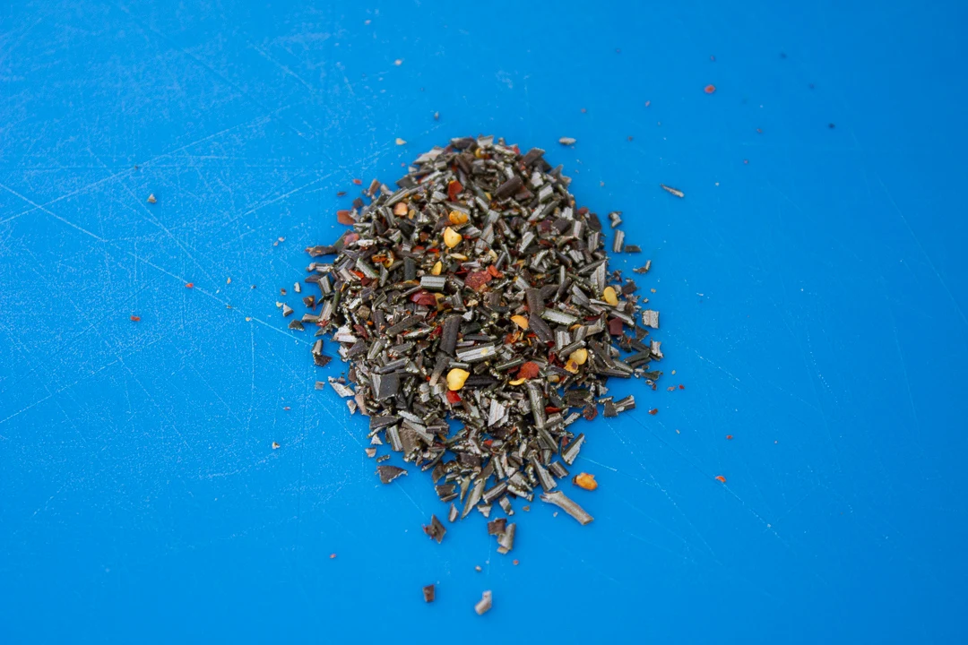 Fresh rosemary and chilli flakes chopped together on a chopping board.