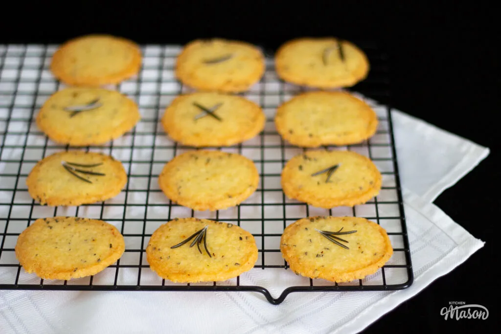 A batch of spicy rosemary crackers on a wire rack over a white tablecloth.