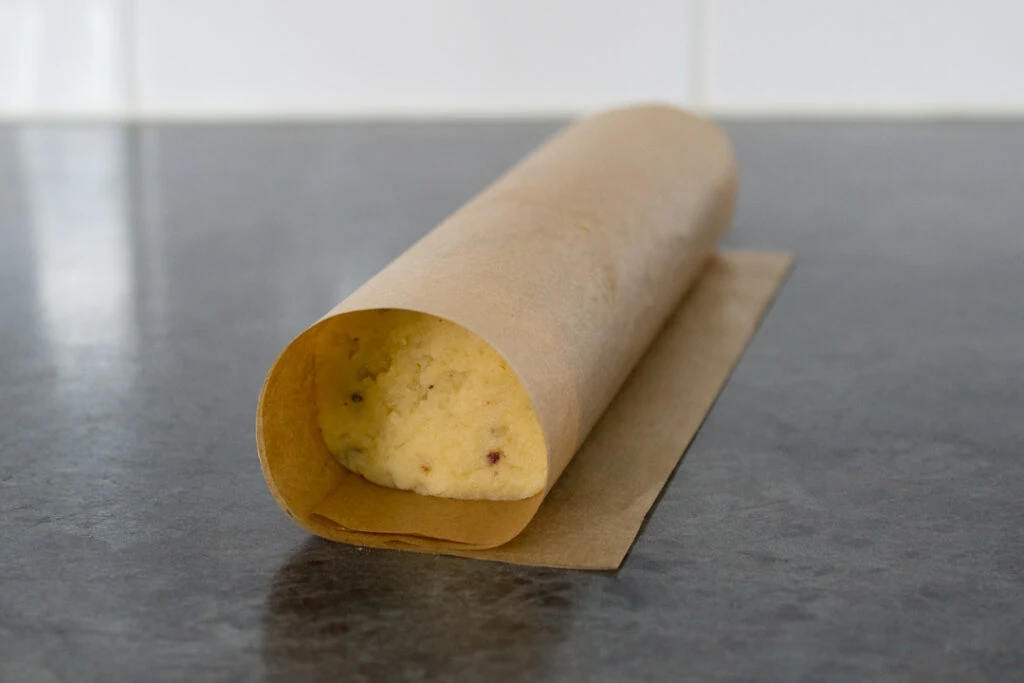 Cracker dough rolling into a cylinder wrapped in baking paper.