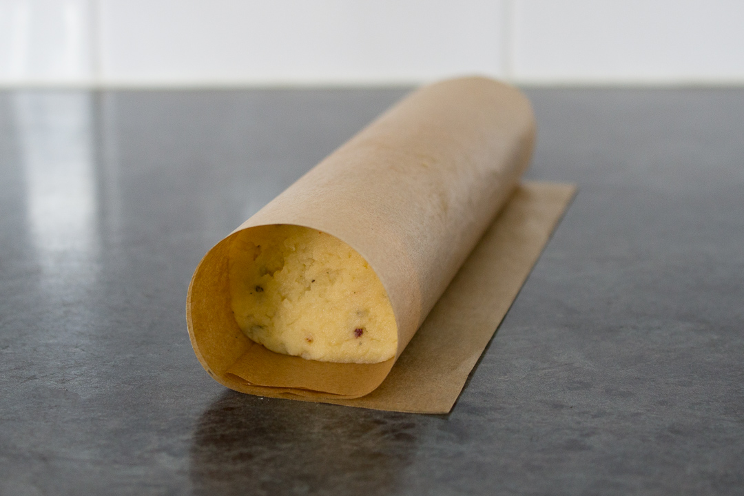 Cracker dough rolling into a cylinder wrapped in baking paper.