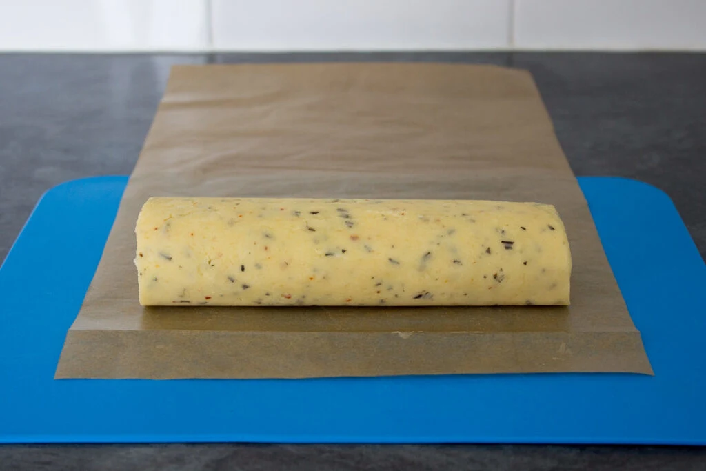 Chilled cylindrical shaped cracker dough on a chopping board.