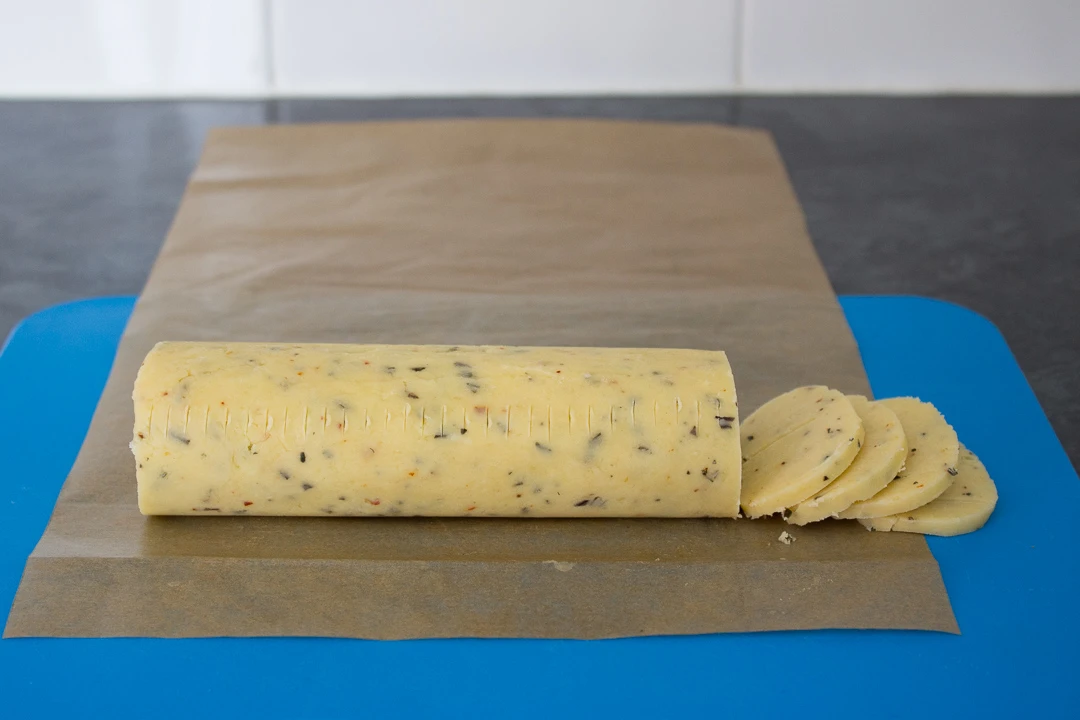 A chilled log of cracker dough being sliced into discs.